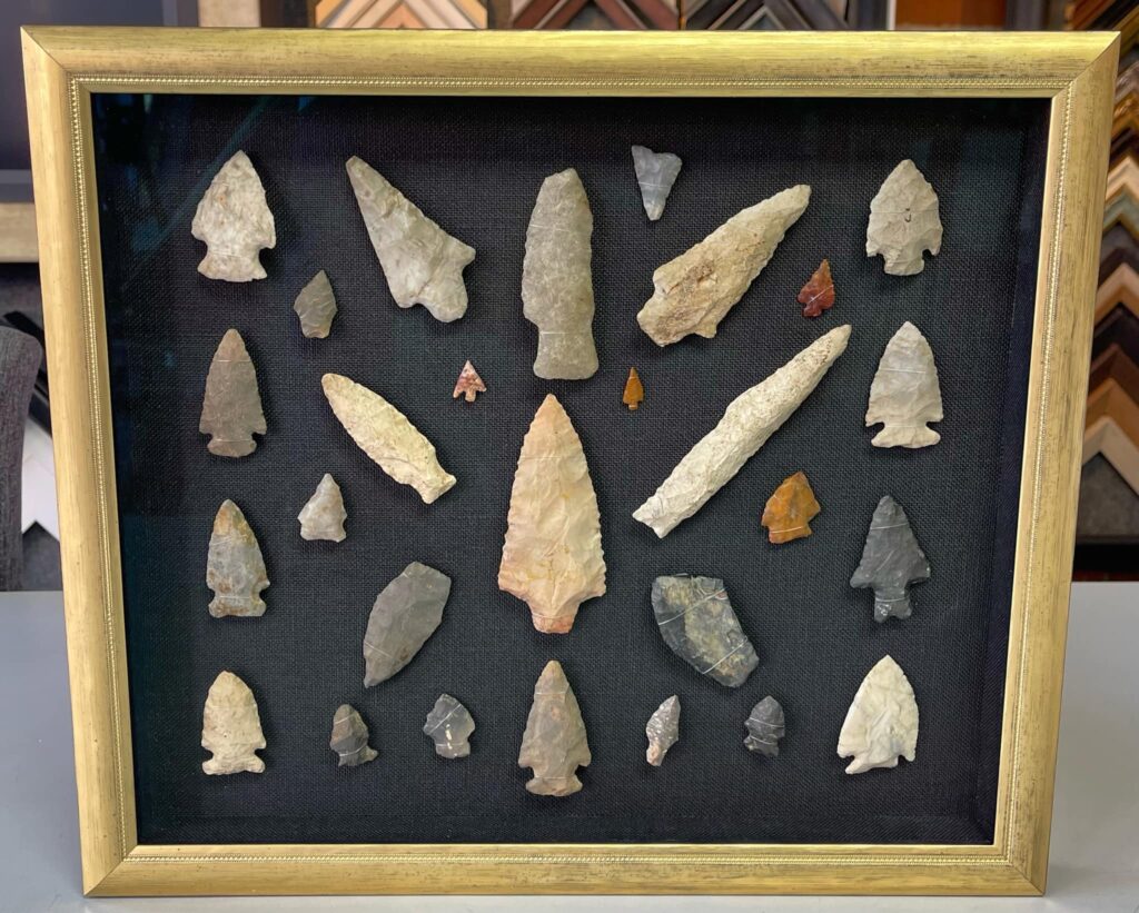 Collection of Native American arrowheads displayed in a custom gold shadowbox frame with black fabric backing